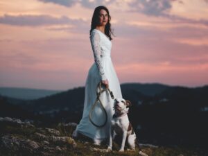 woman wearing white lace gown with dog sitting on the ground
